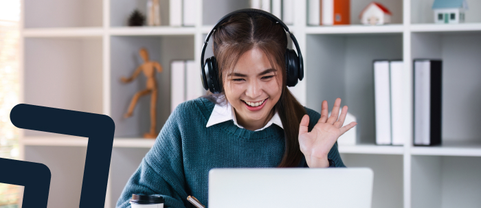 Estudiante con audífonos sonríe y saluda a profesor en clase virtual a través de su laptop