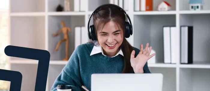 ​Estudiante con audífonos sonríe y saluda a profesor en clase virtual a través de su laptop​