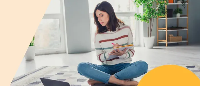 ​Mujer universitaria en clase virtual toma apuntes en una libreta​